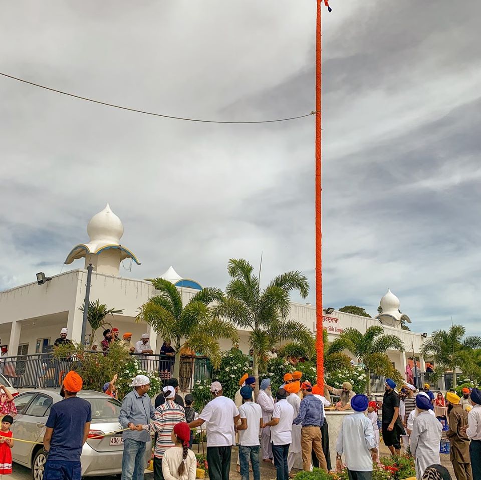 Sangat gathered around the Nishan Sahib outside the Gurdwara